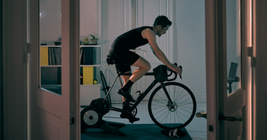 Man training on indoor bicycle in a darkened home office