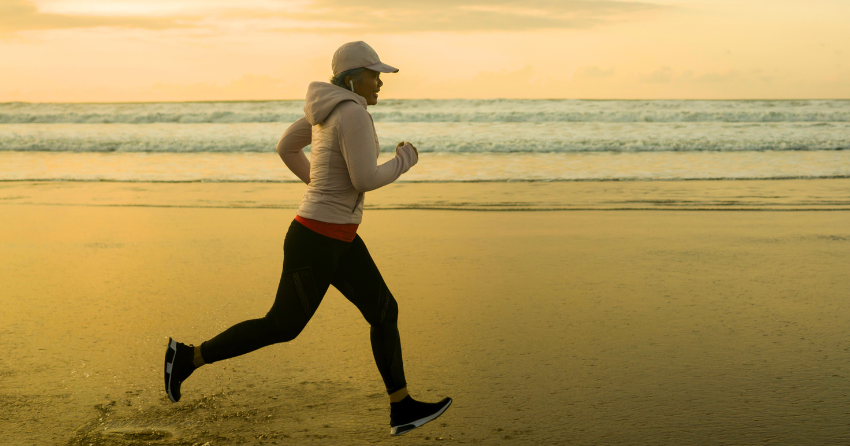 Healthy and active middle aged woman running powerfully on a beach at sunrise